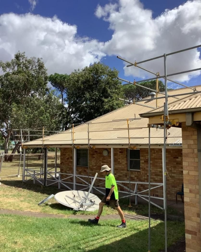 A Man Is Walking in Front of A House with Scaffolding on The Roof — Site Safety NSW in Lake Macquarie, NSW