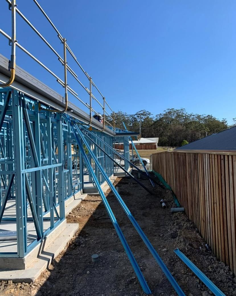 A Blue Metal Structure Is Being Built Next to A Wooden Fence — Site Safety NSW in Maitland, NSW