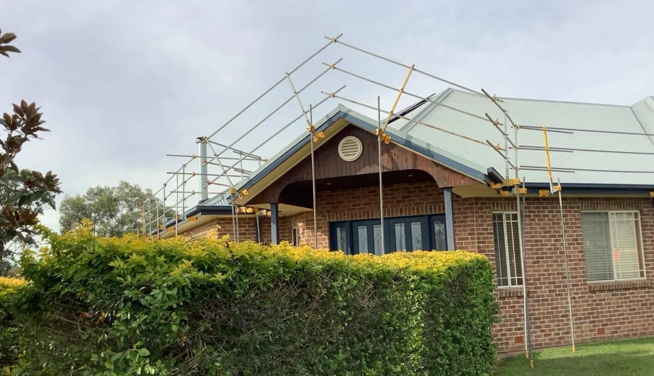 A Brick House with Scaffolding on The Roof and A Hedge in Front of It — Site Safety NSW in Sandgate, NSW