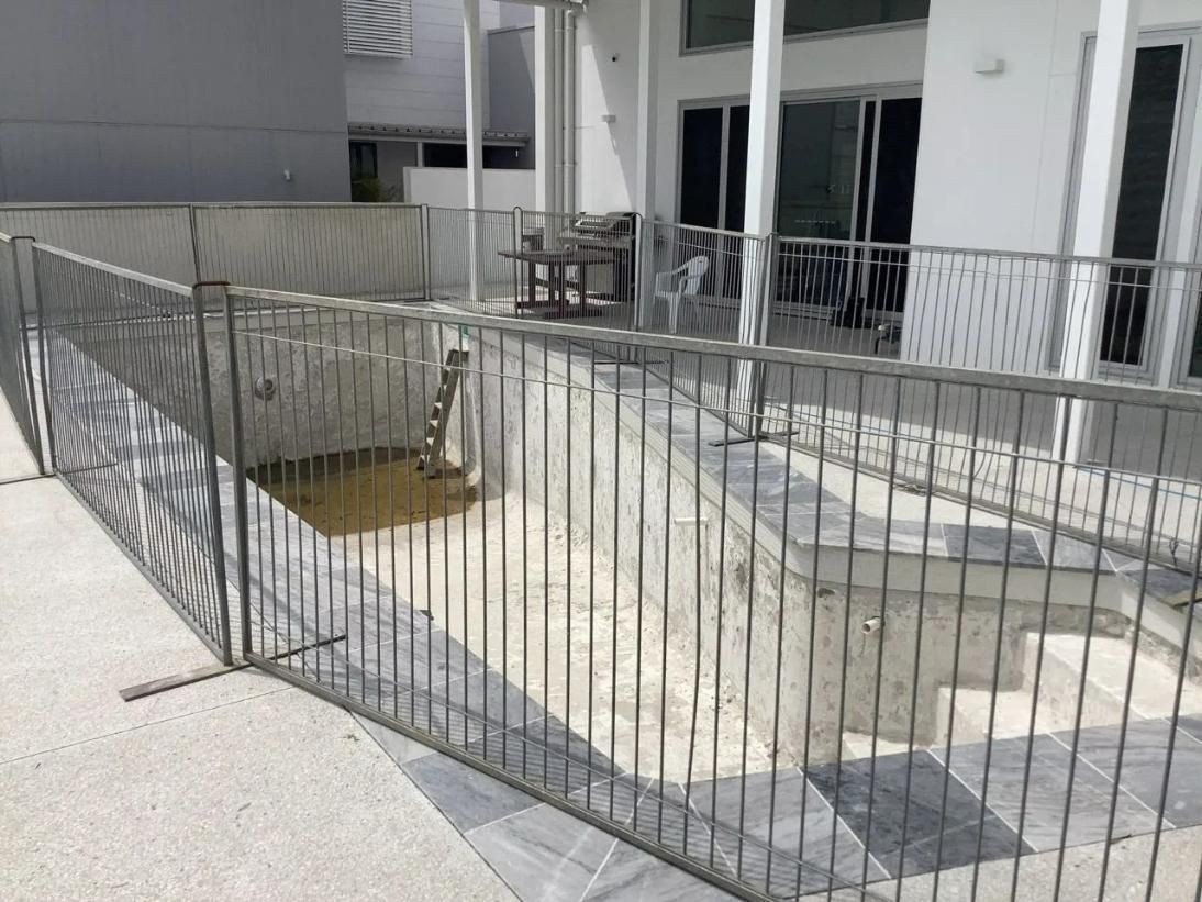 A Metal Fence Is Surrounding a Swimming Pool in Front of A House — Site Safety NSW in Sandgate, NSW