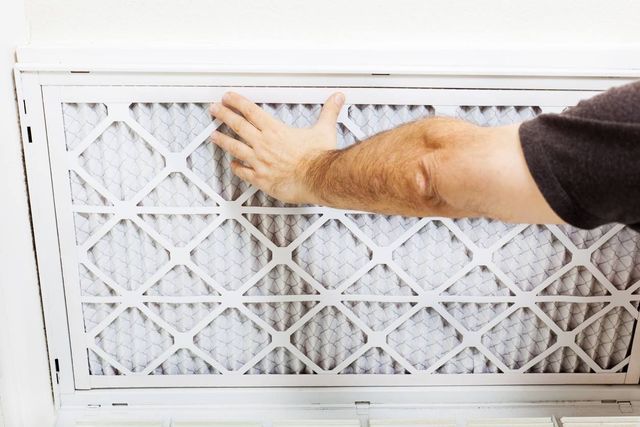 Person replacing an air filter in a white frame. Hand touches the filter, which has a grid pattern.