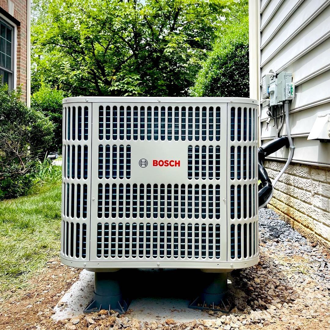 Bosch air conditioning unit outside a house, surrounded by grass and gravel.