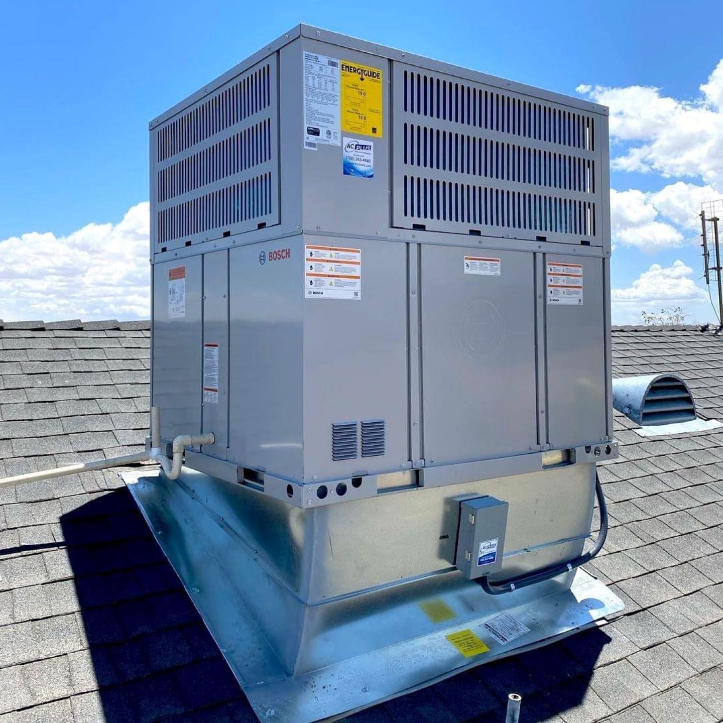 Rooftop HVAC unit, gray metal, with vents, sitting on gray shingles, against a blue sky.