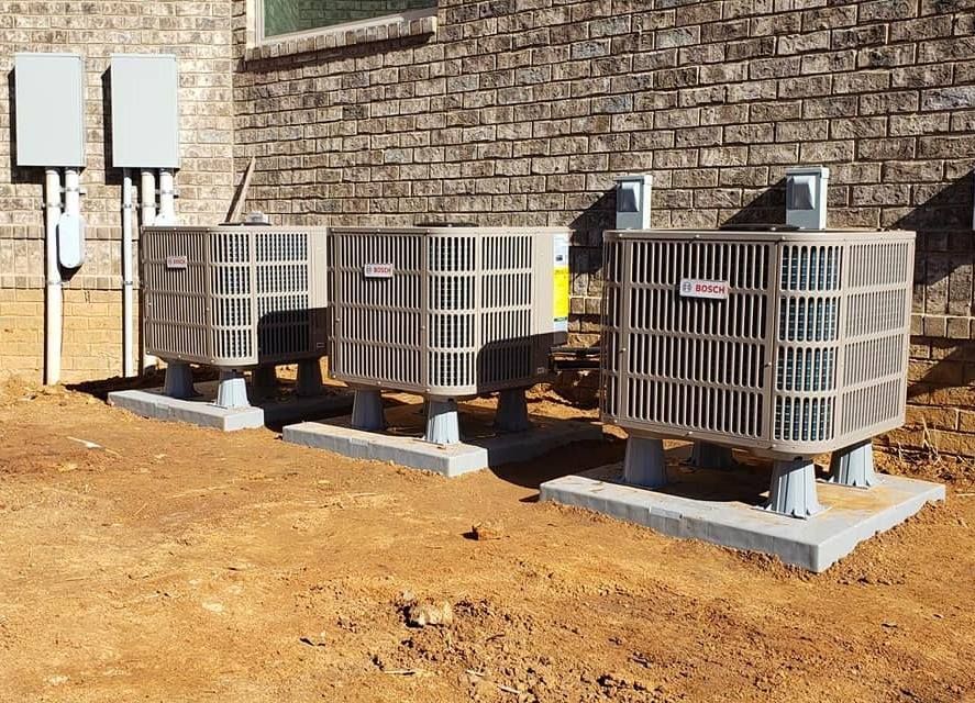 Three air conditioning units on concrete pads next to a brick building.