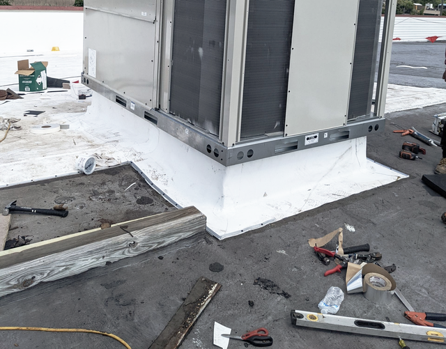 HVAC unit on a rooftop with white sealant around the base, surrounded by tools.