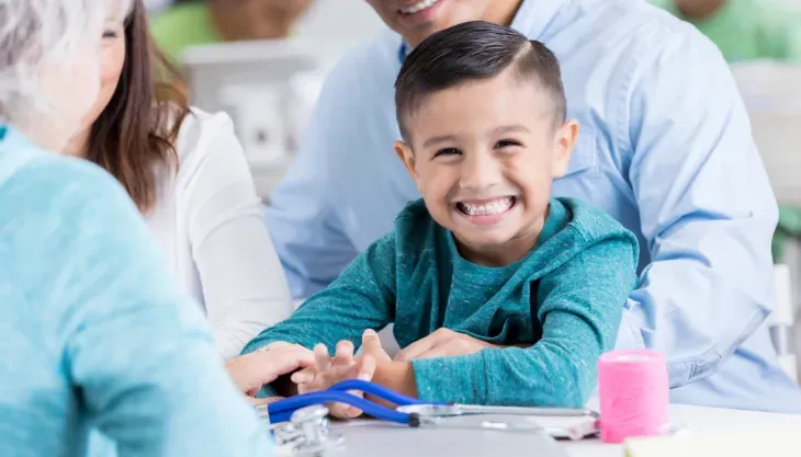 A young boy is sitting at a table with his parents and a doctor.