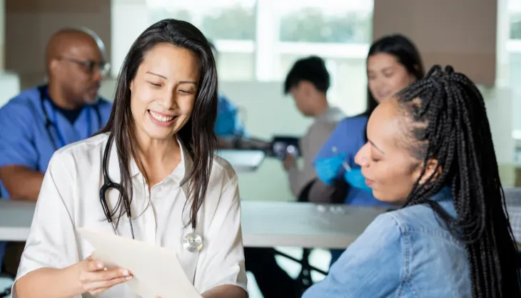 A nurse is talking to a patient while holding a clipboard.