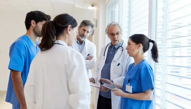 A group of doctors and nurses are standing in a room talking to each other.
