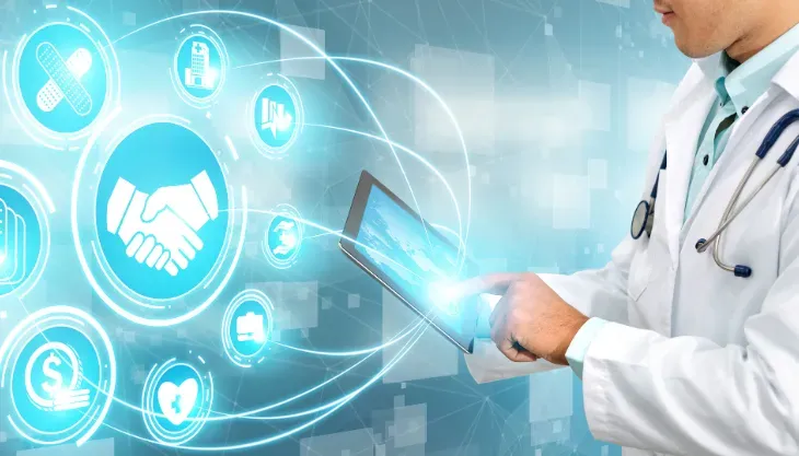 A doctor is using a tablet computer with a handshake icon on the screen.