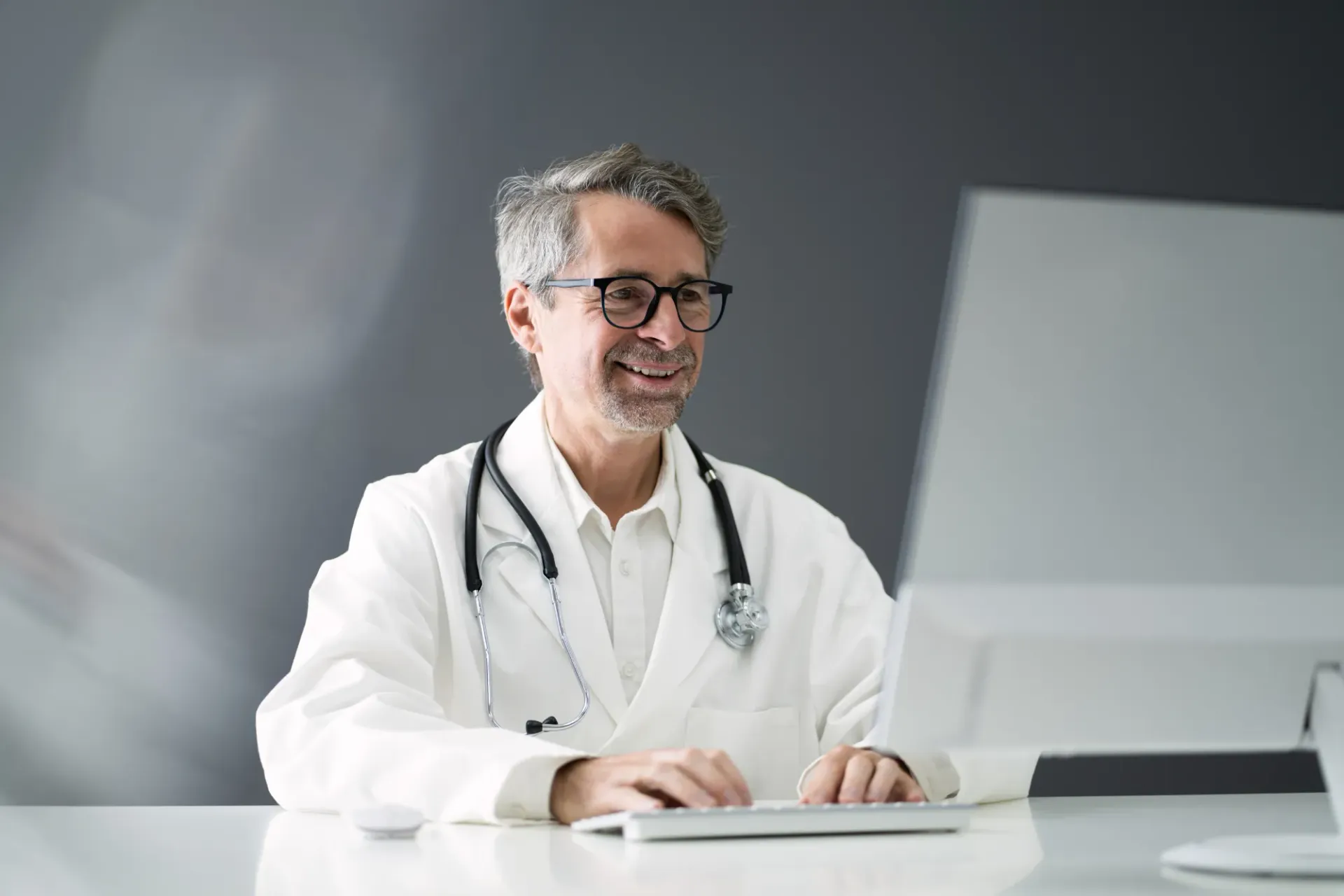 A doctor is sitting at a desk in front of a computer.