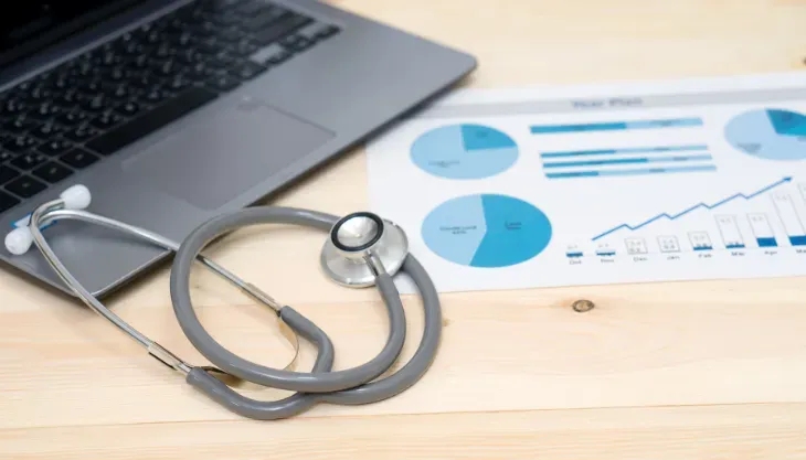 A stethoscope is sitting next to a laptop on a wooden table.