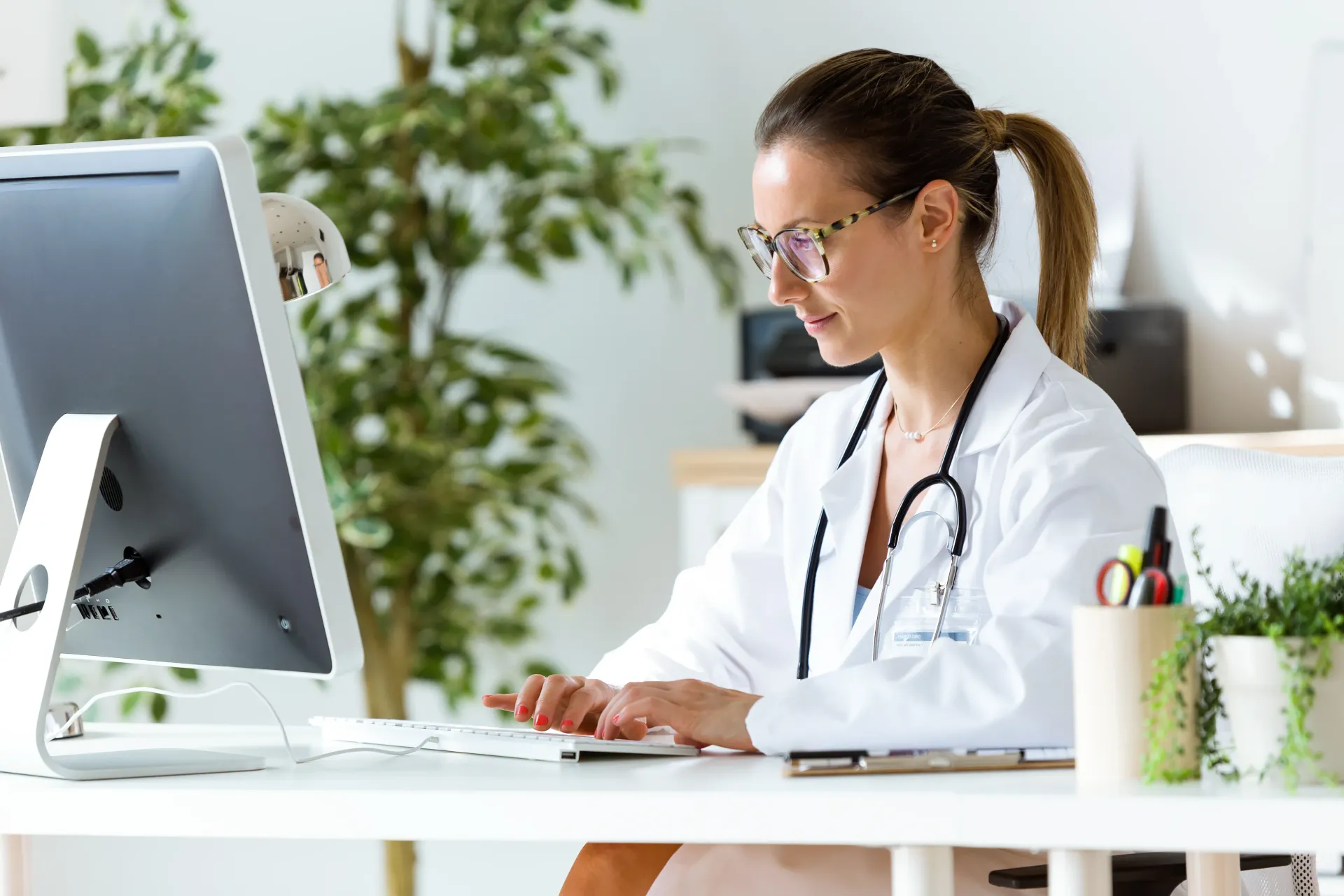 A female doctor is sitting at a desk in front of a computer.
