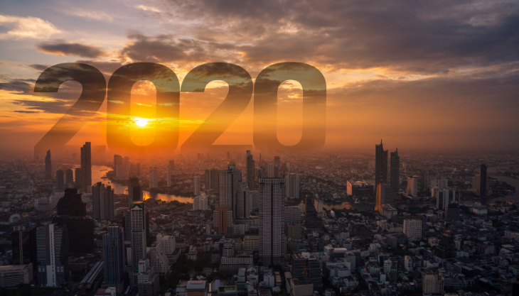 The year 2020 is written in the sky over a city at sunset.
