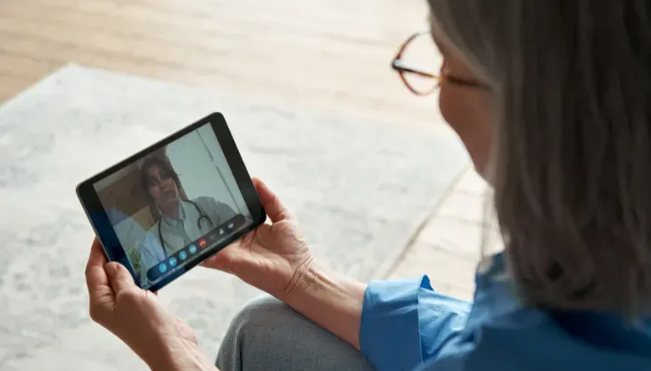 A woman is holding a tablet and having a video call with a doctor.