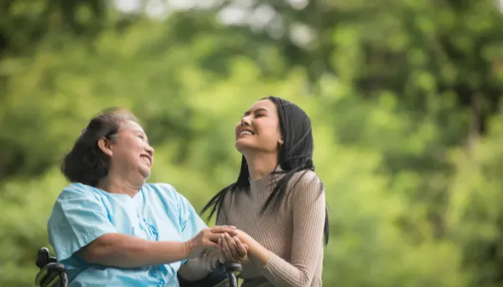 A woman in a wheelchair is holding the hand of another woman.