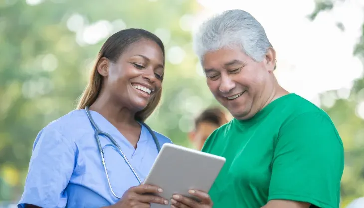 A nurse and a man are looking at a tablet together.