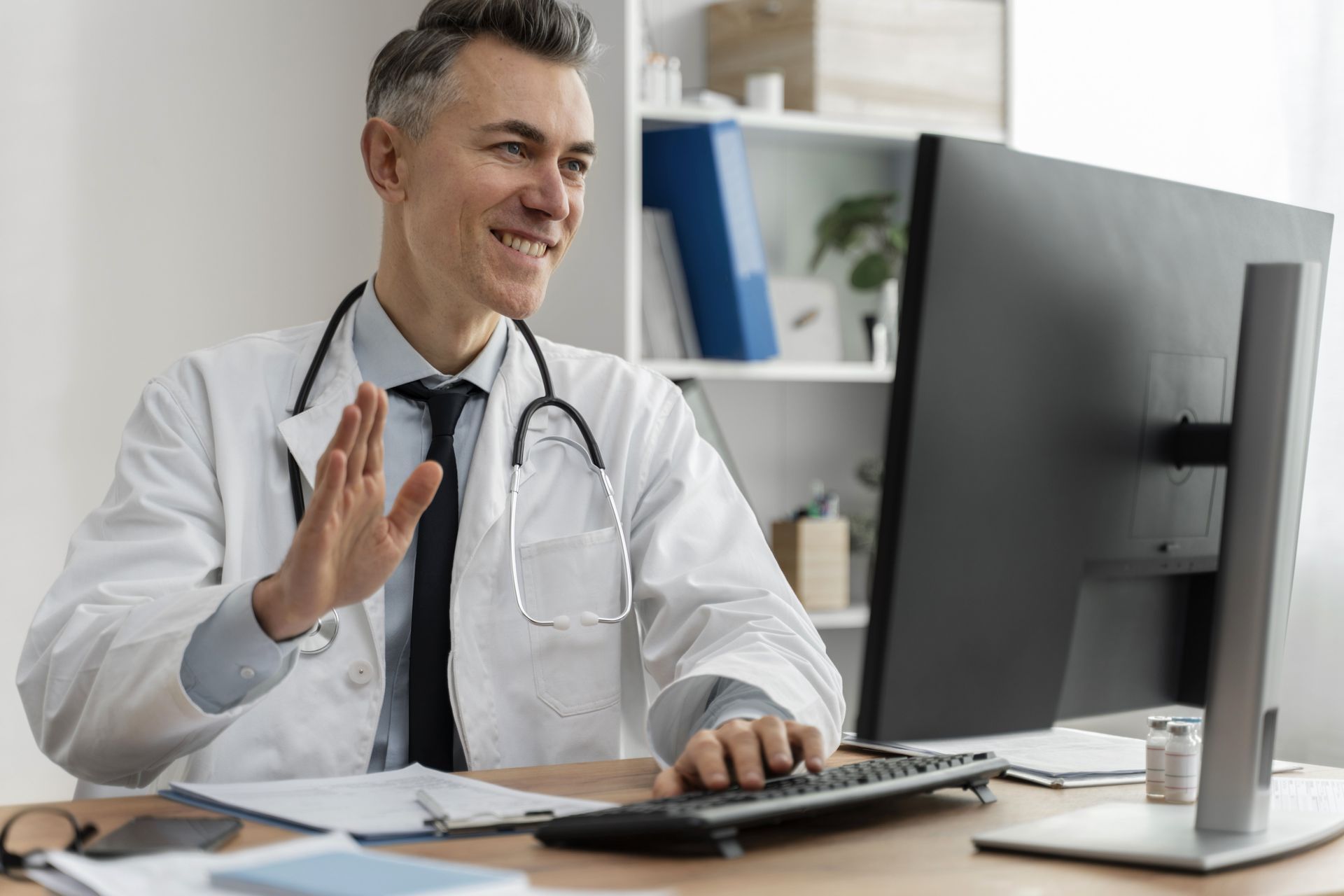 A doctor is sitting at a desk in front of a computer.