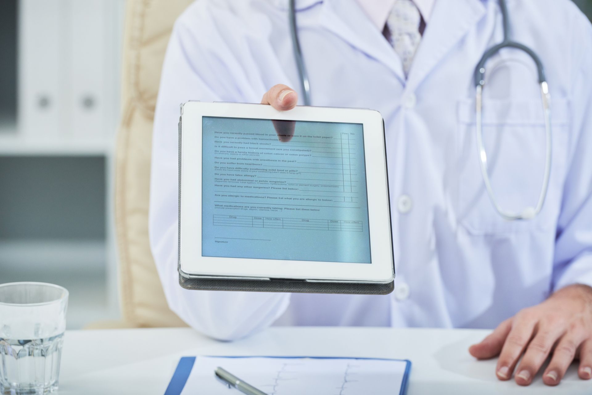 A doctor is sitting at a desk holding a tablet computer.