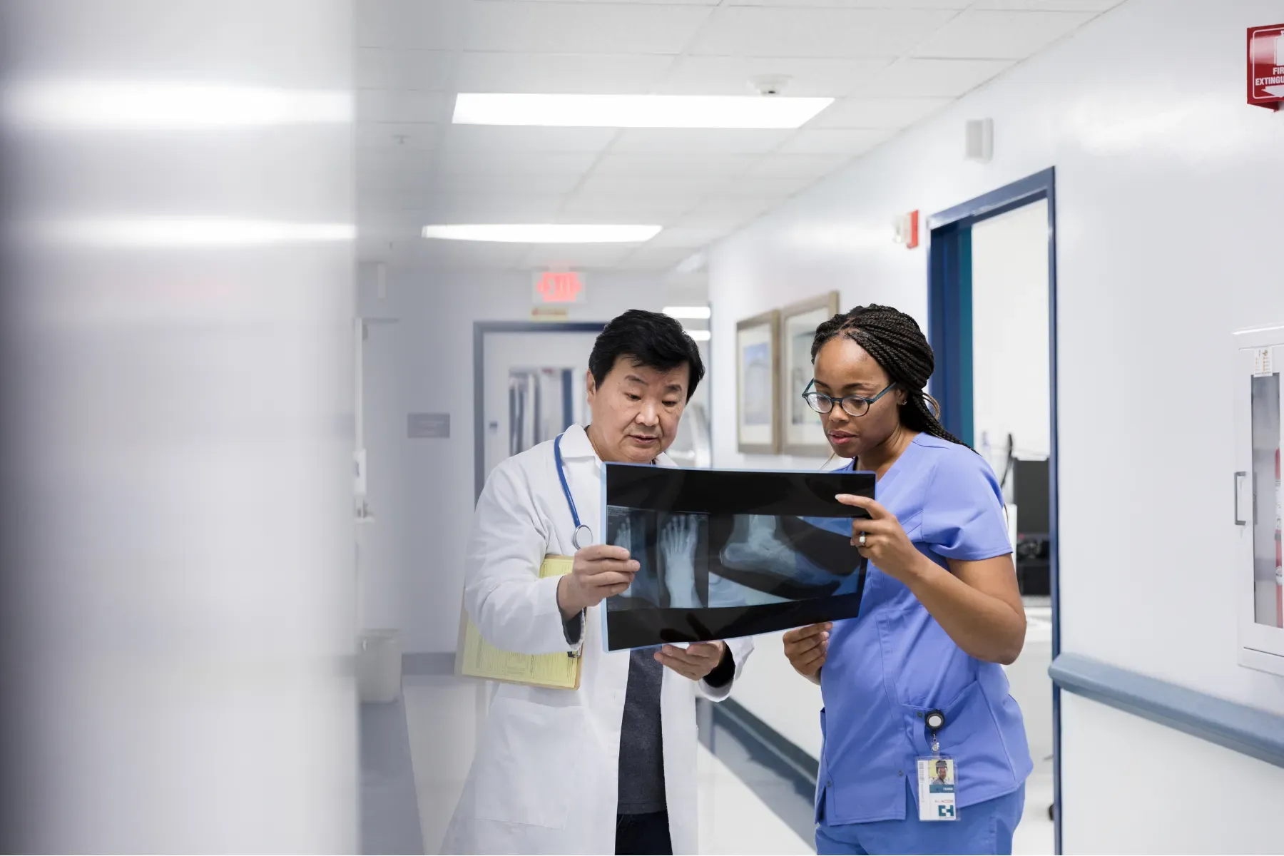 A doctor and a nurse are looking at an x-ray in a hospital hallway.
