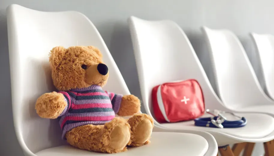 A teddy bear is sitting on a chair in a waiting room.