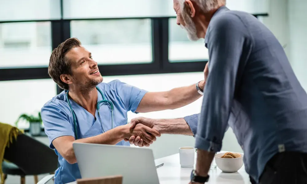 A doctor is shaking hands with an older man while sitting at a table.