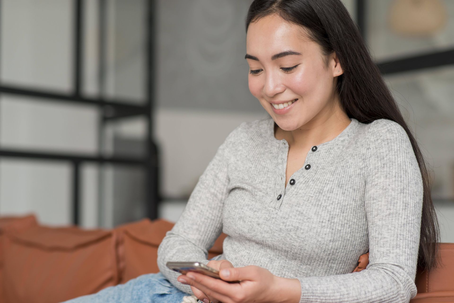 A woman is sitting on a couch using a cell phone.