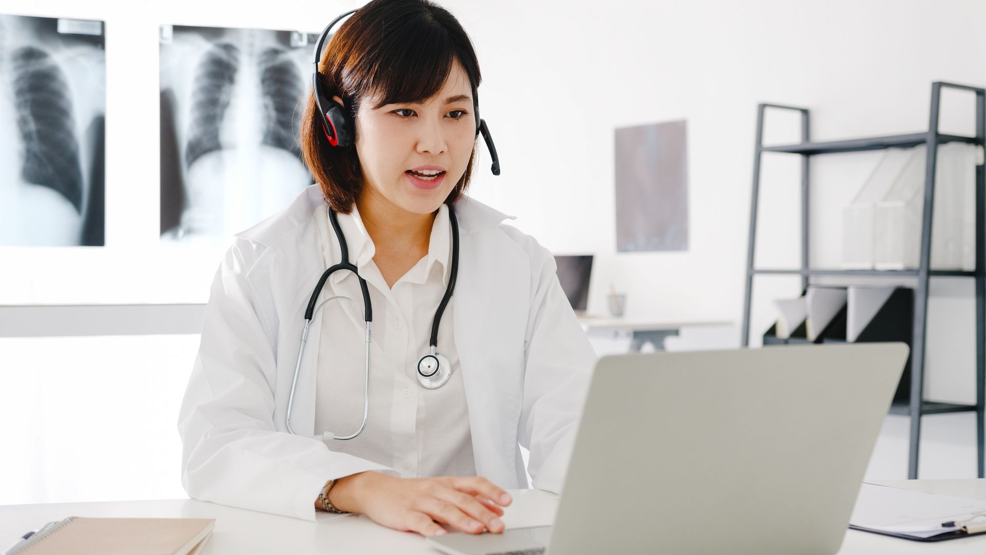A female doctor wearing a headset is sitting in front of a laptop computer.