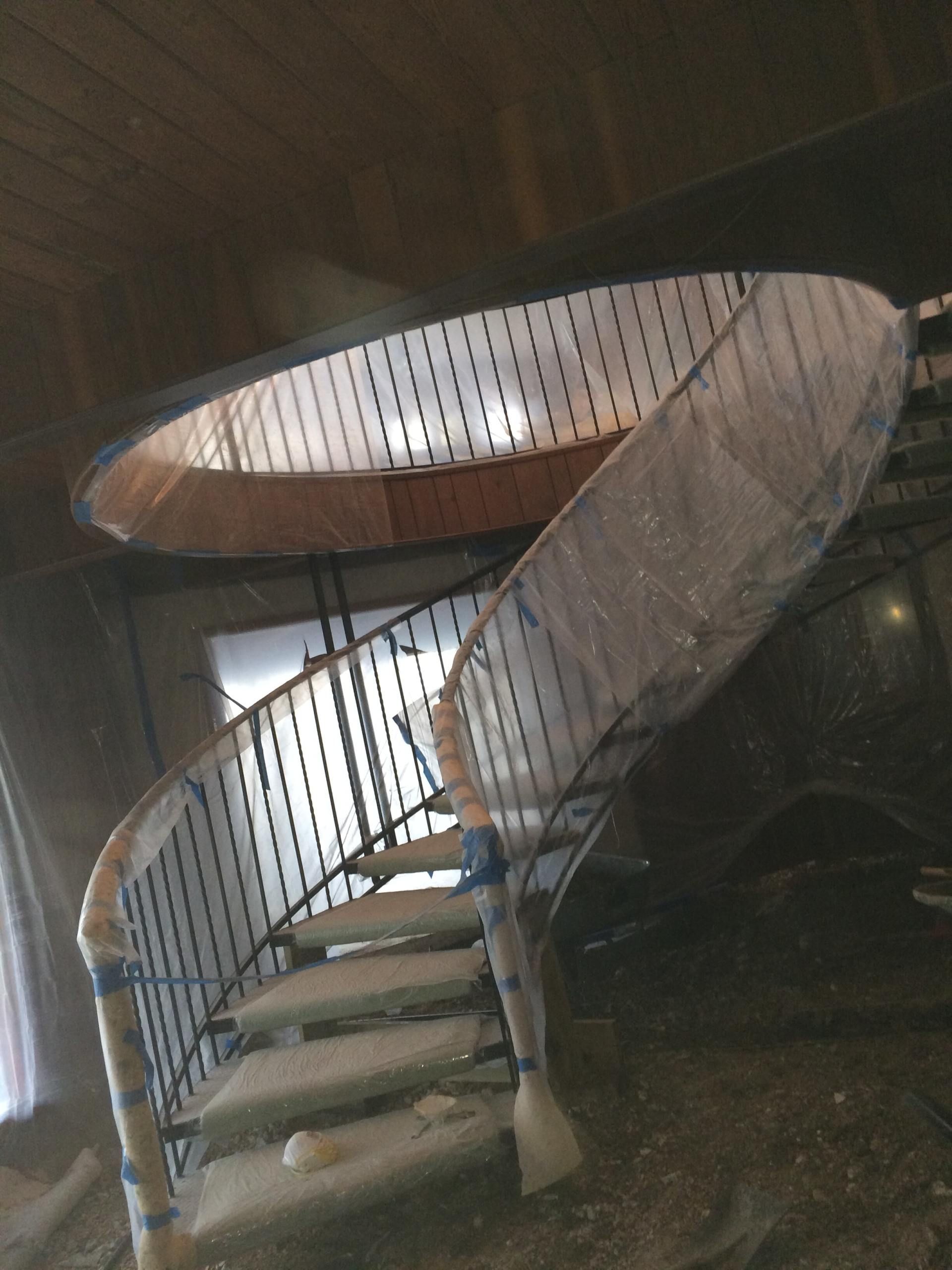 Spiral staircase with black iron railing and steps covered in protective wrap.