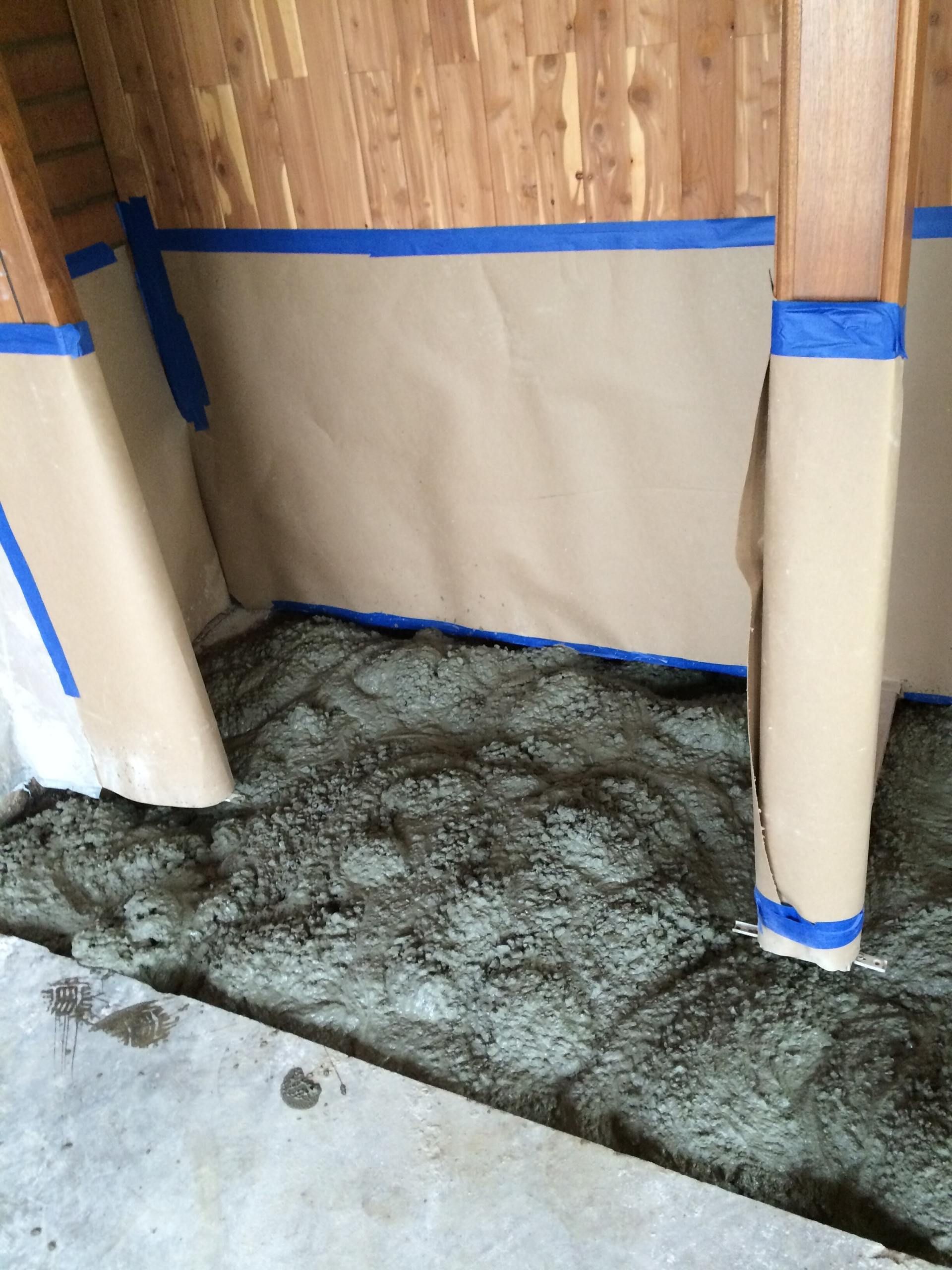Brown paper taped to beams, surrounding wet cement. Concrete floor.