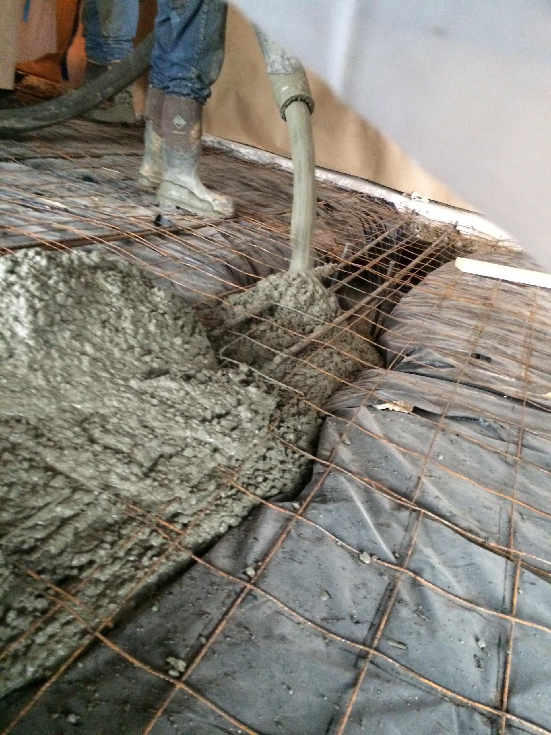 Concrete being poured onto rebar mesh and black sheeting by a construction worker.