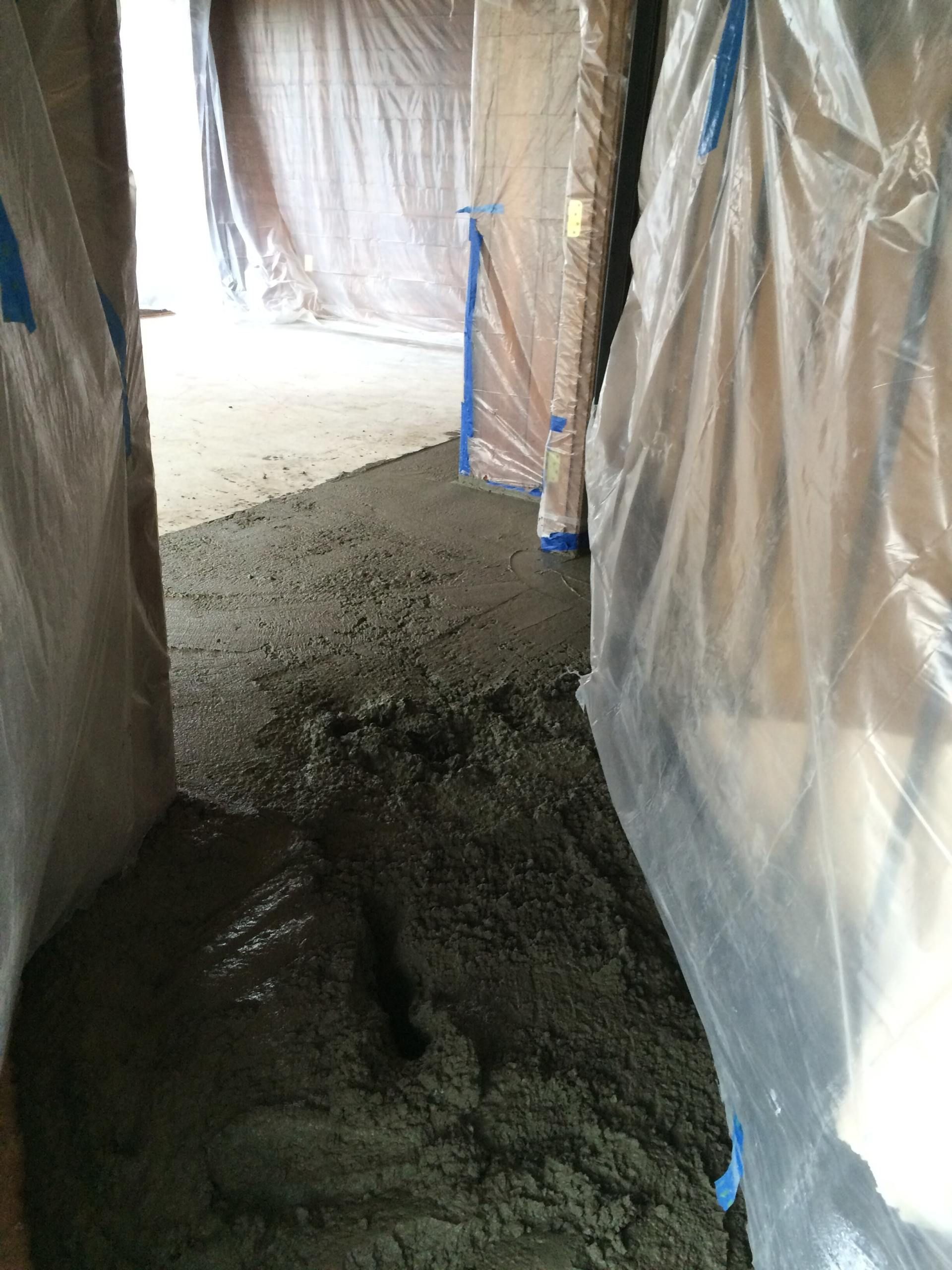 Concrete floor being poured in a construction site, with plastic sheeting protecting the walls.