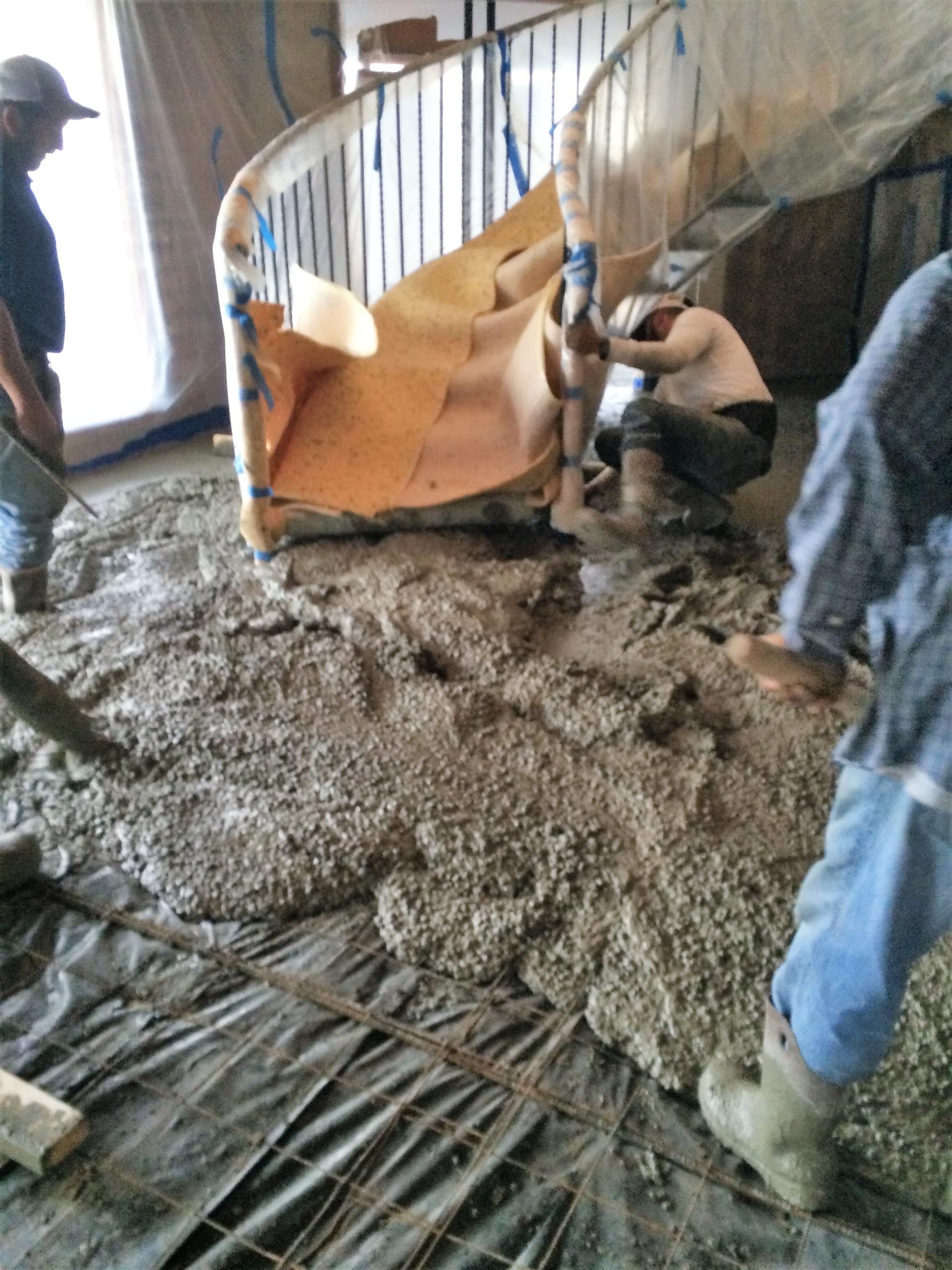 Construction workers pouring wet concrete around a curved staircase.