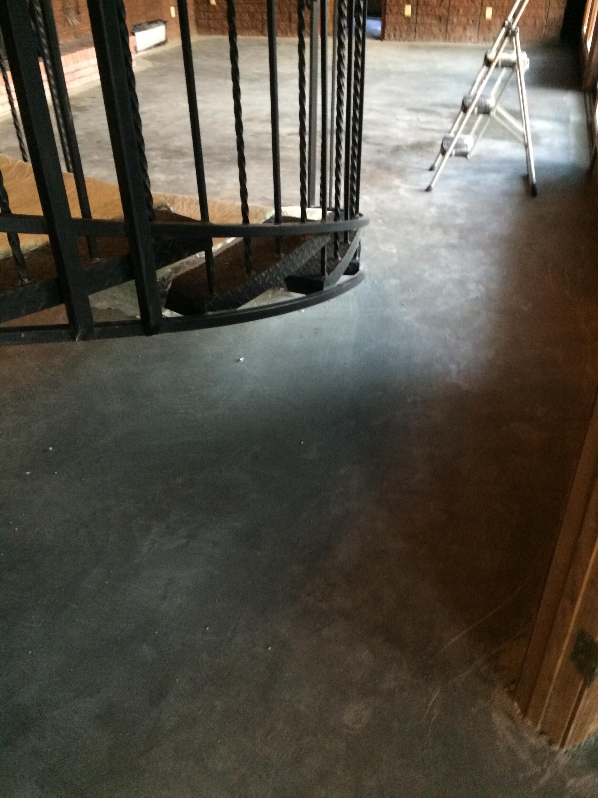 Black iron railing curving down to gray concrete floor; stepladder in background.