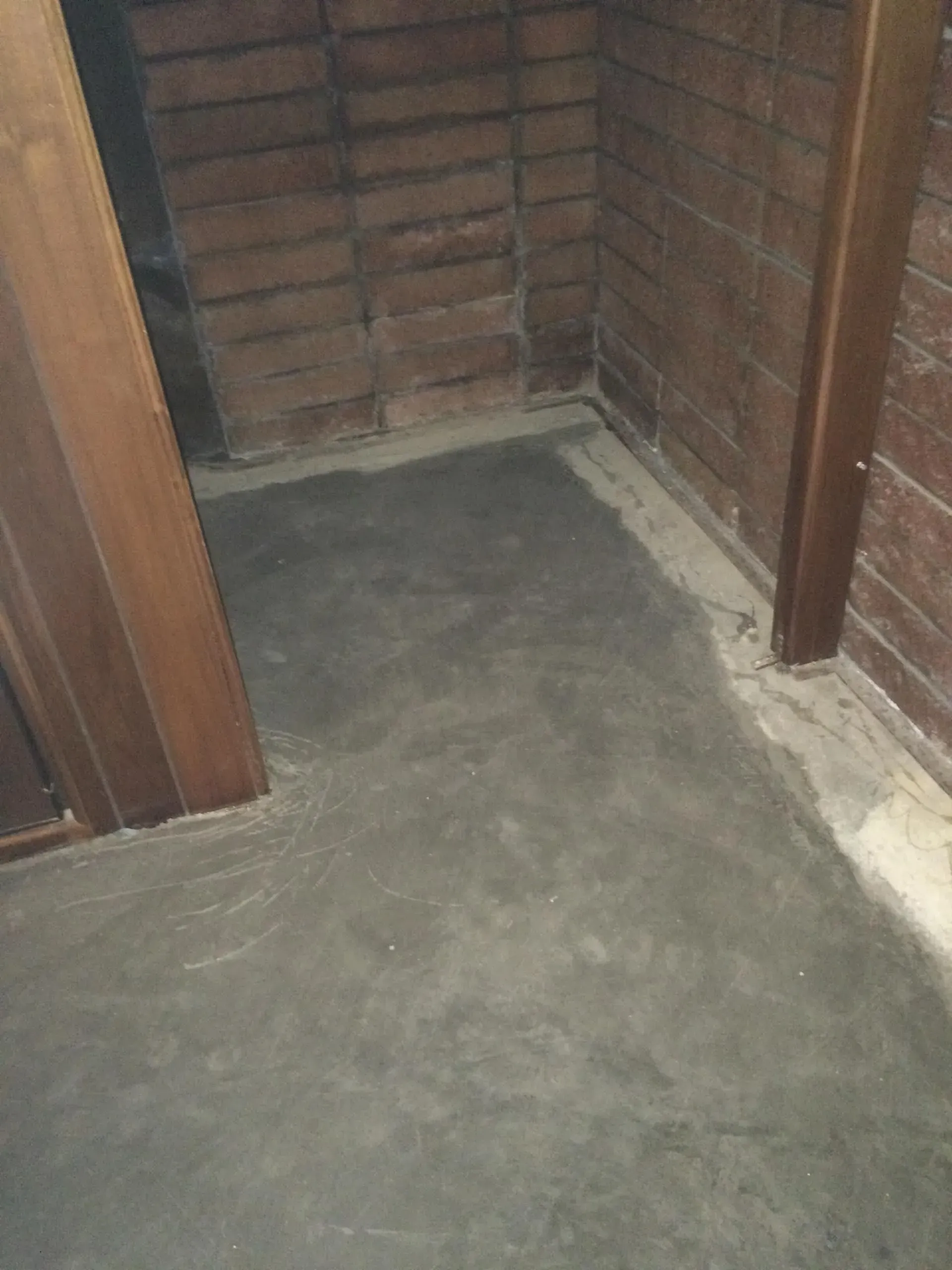 A freshly leveled concrete floor in a small room with brick walls and wooden door frames. A freshly leveled concrete floor in a small room with brick walls and wooden door frames.