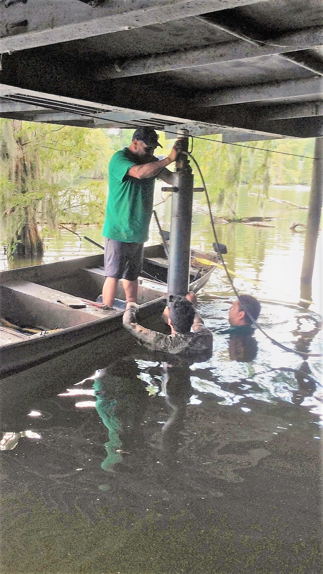 Man on boat helps two people in water near a bridge, possibly working.