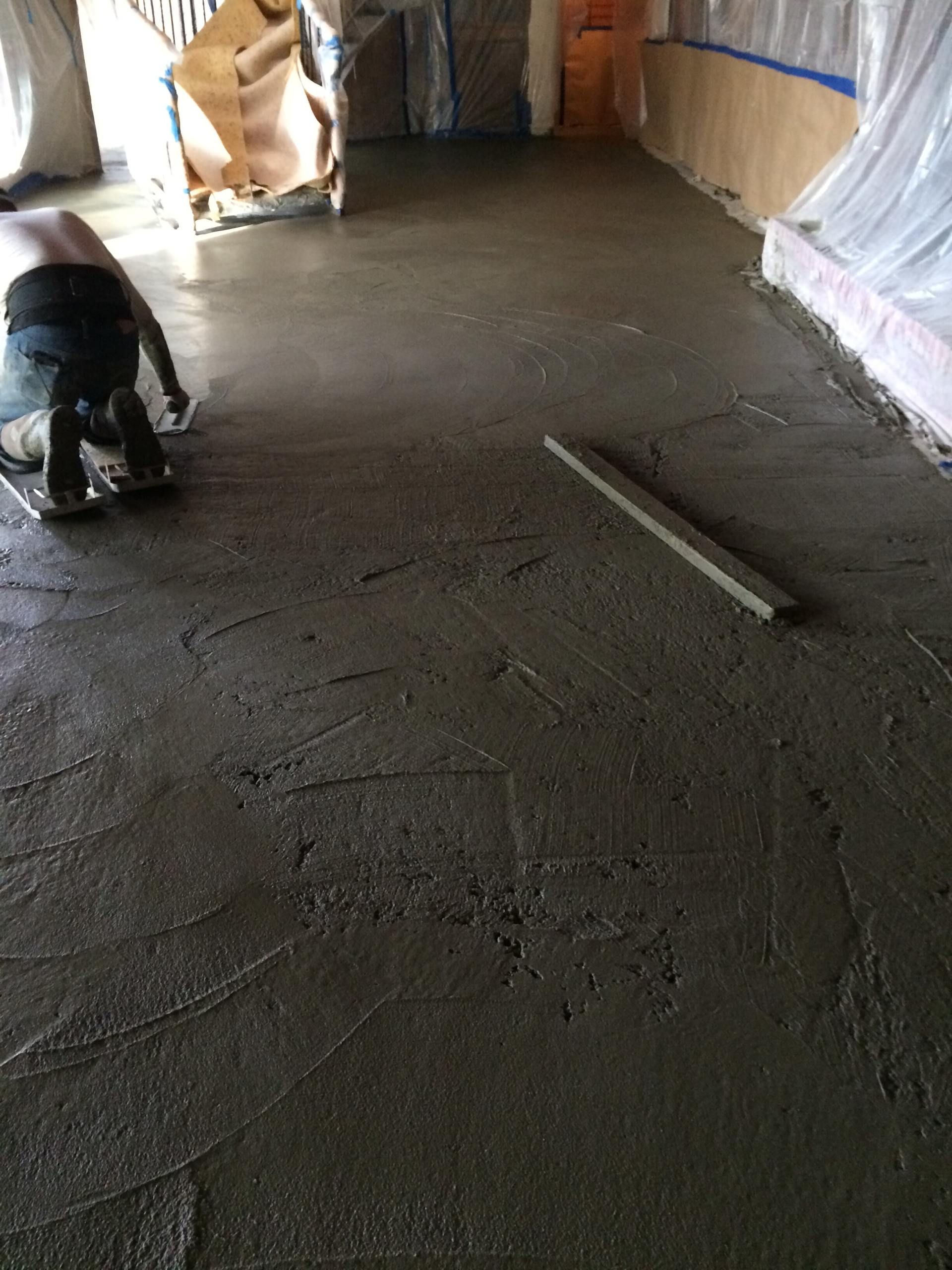 Man smoothing wet concrete floor with a trowel indoors, creating a level surface.