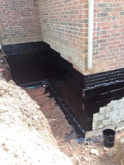 Foundation waterproofing with black sealant on a brick wall.
