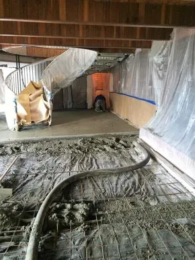 Concrete being poured in a basement, a worker is visible inside a doorway.