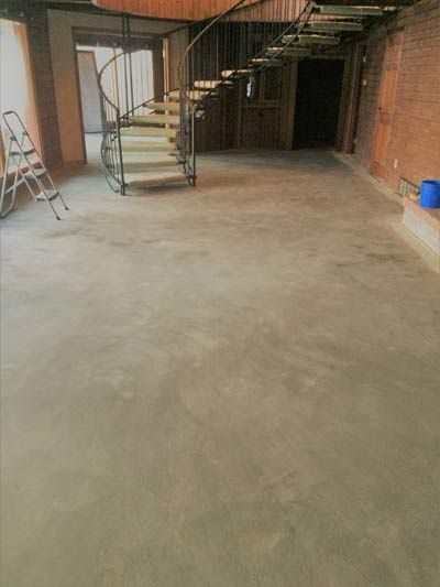 Empty room with spiral staircase and concrete floor; ladder leaning against a wall.