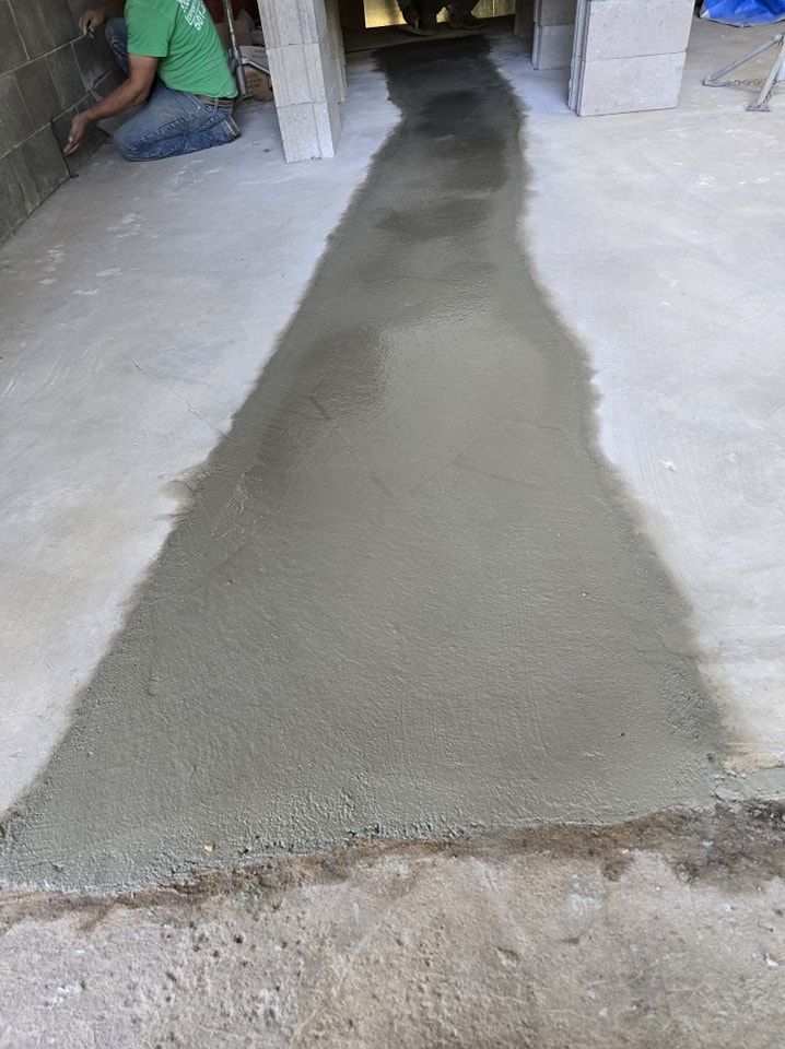 Person smoothing fresh concrete path between cinder block structures.