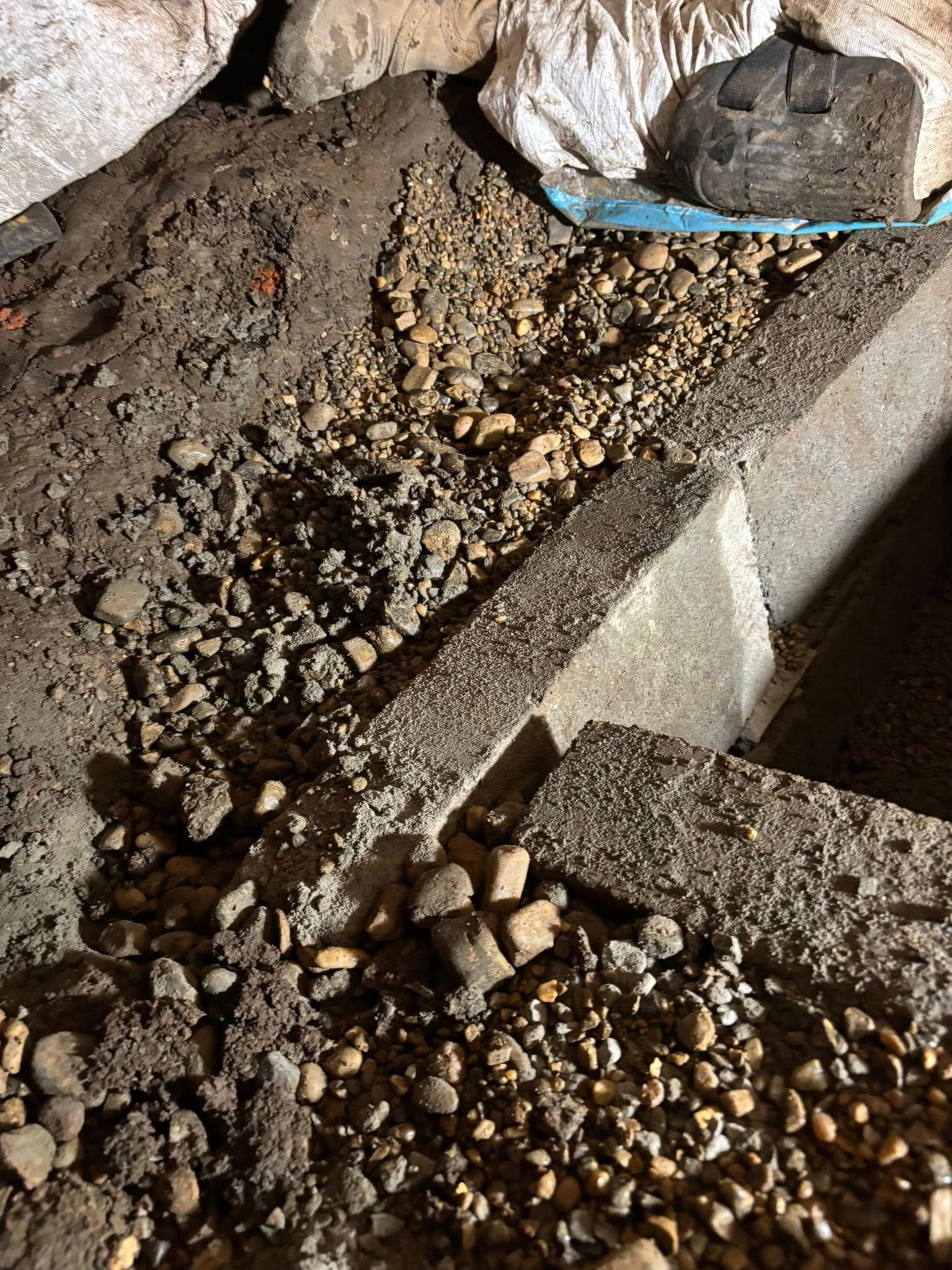 Dirt and gravel in a crawlspace, including a concrete foundation.