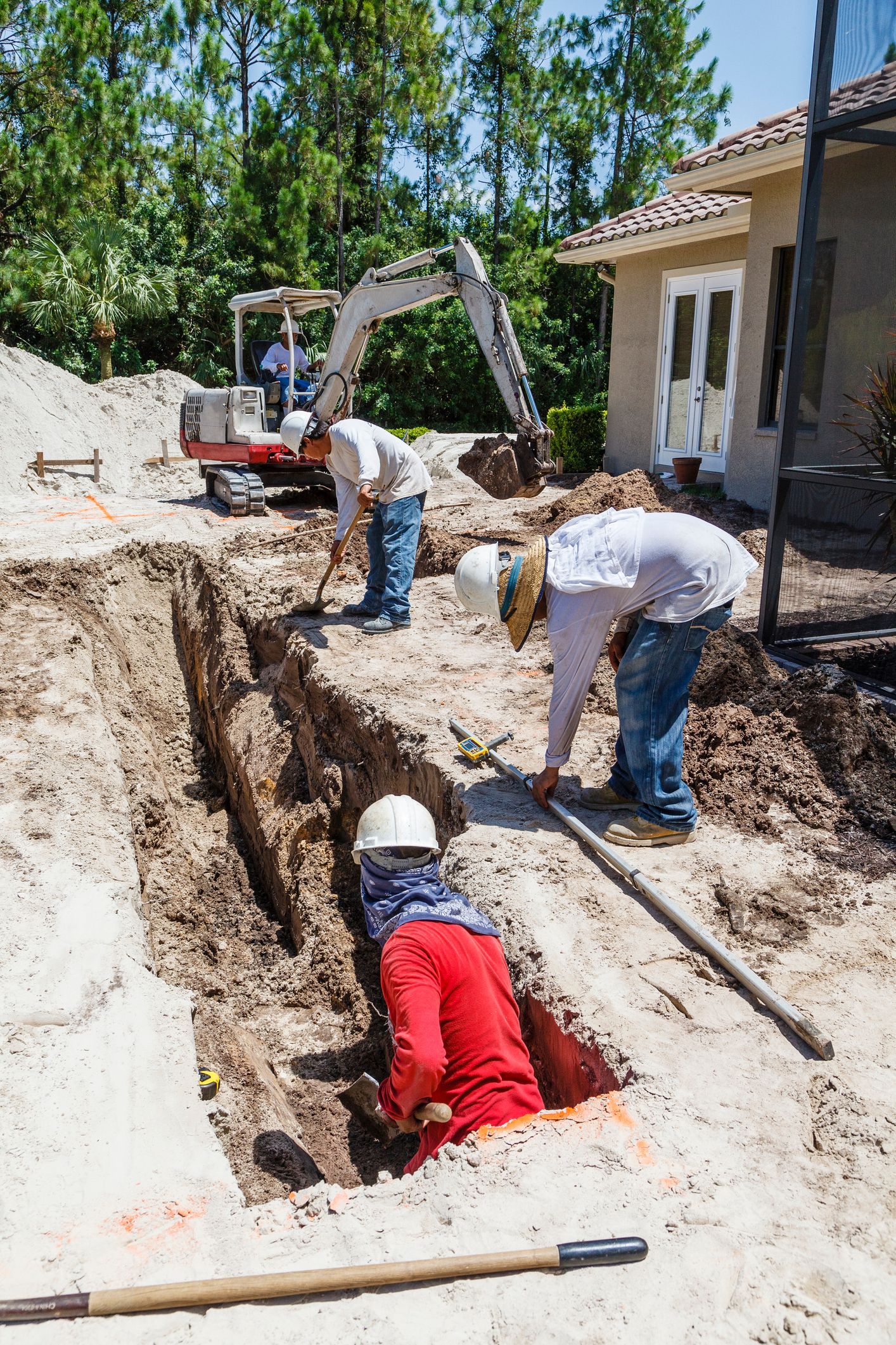 A trench dug in a yard with retaining walls, a backhoe in the background, and leaves scattered throughout.