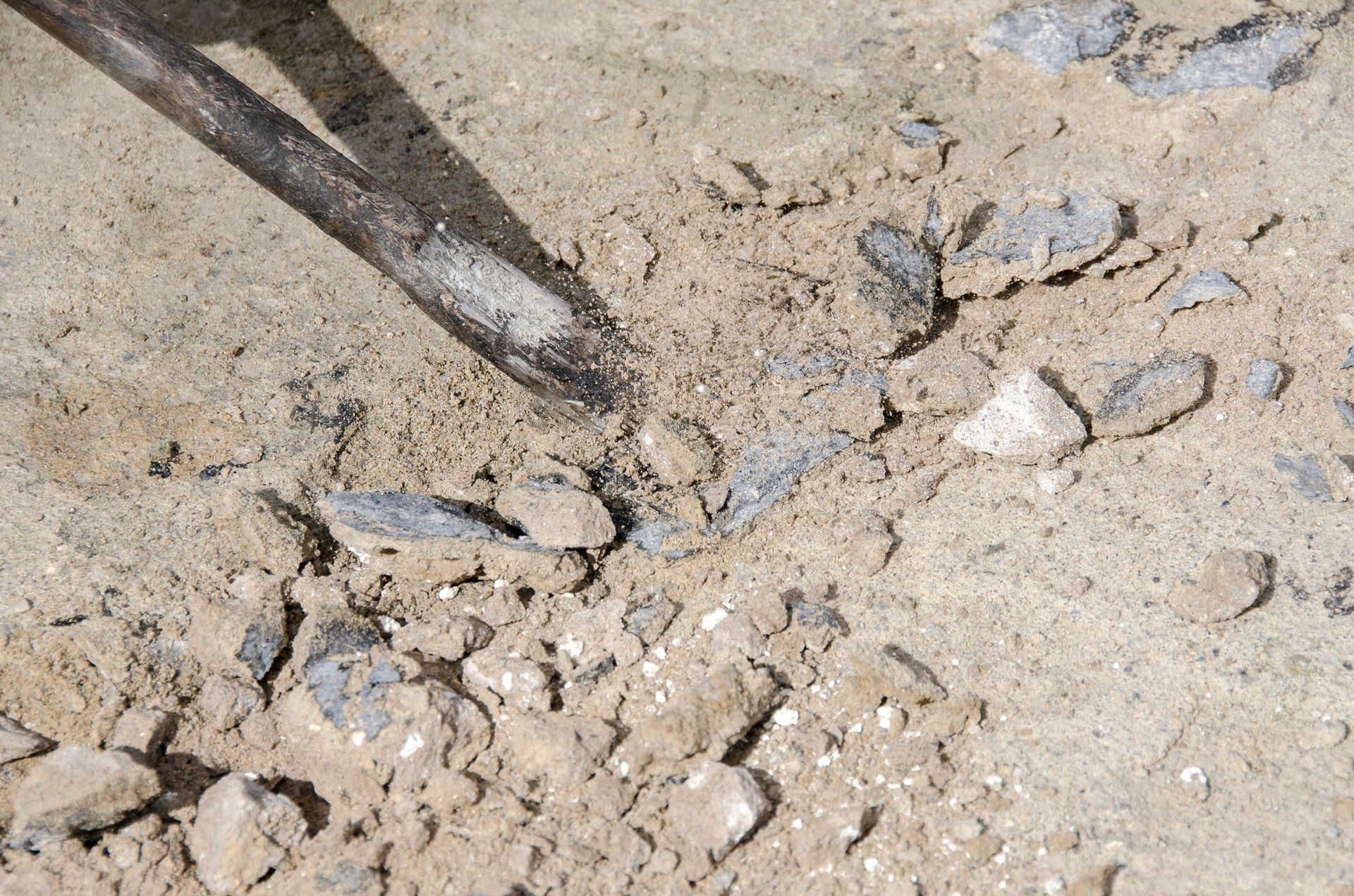 Person in green shirt smoothing wet concrete on a sidewalk, wooden stakes mark the border.