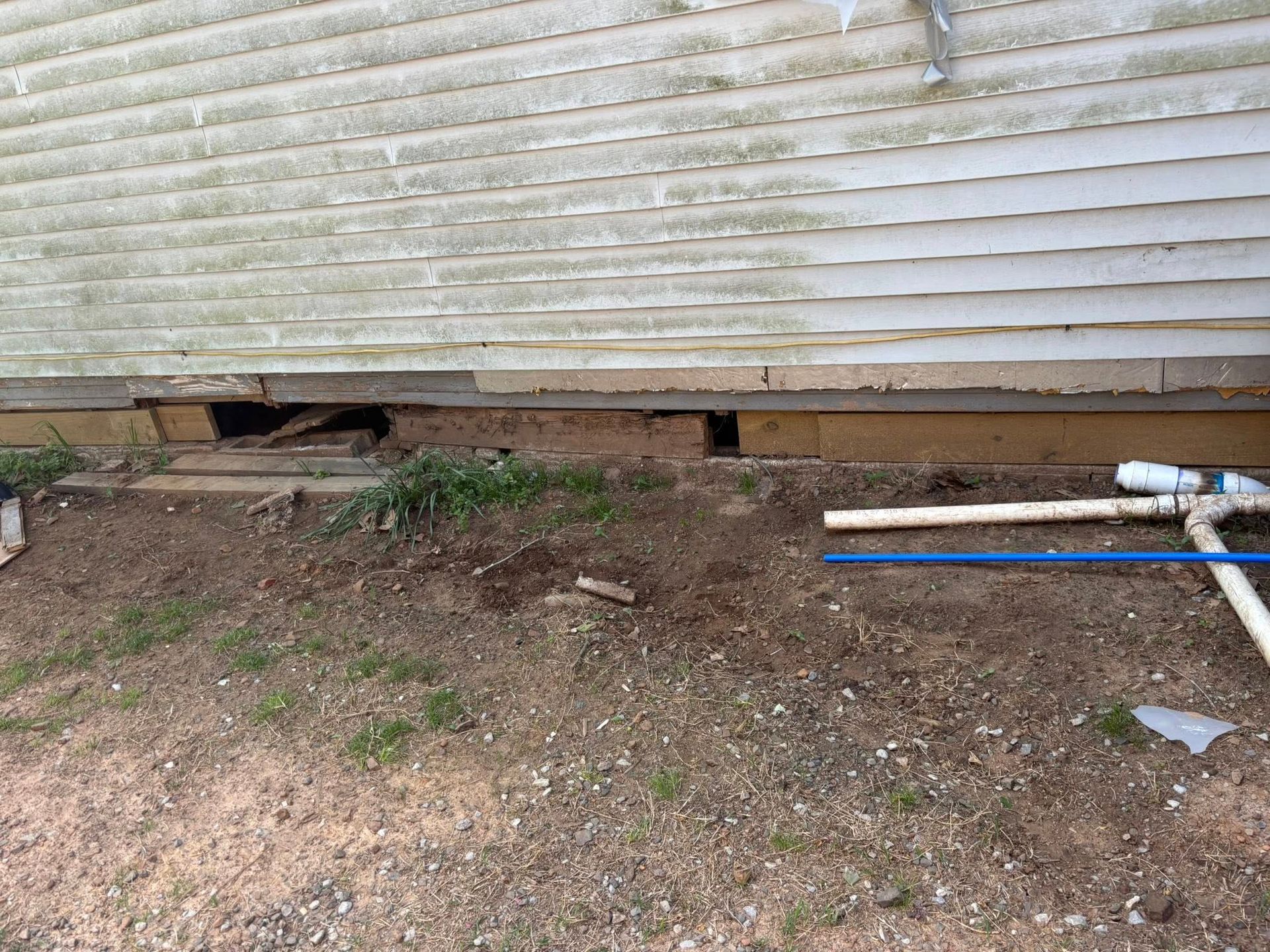 A wooden pier with support beams sits over muddy ground near water. A wheelbarrow and ladder are underneath.