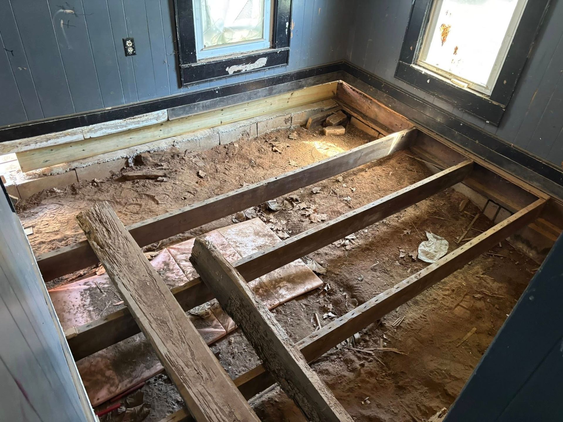 Person installing rebar grid on a dirt patio, next to a house. Green shirt, outside.