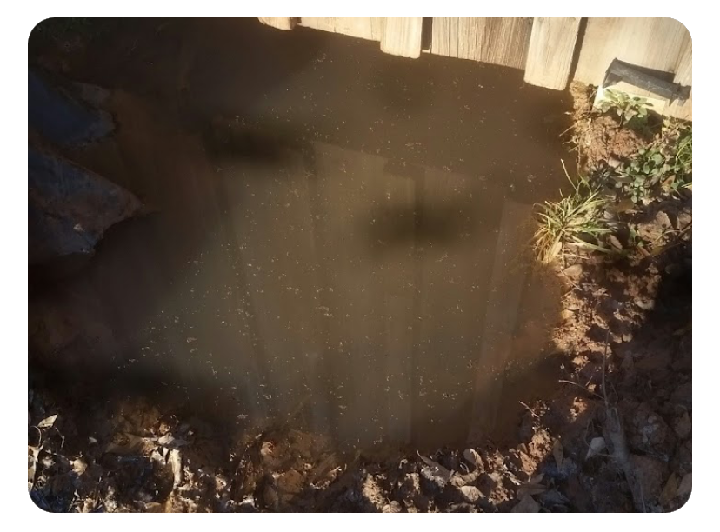 A trench dug in a yard with retaining walls, a backhoe in the background, and leaves scattered throughout.