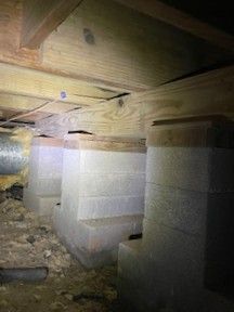 A wooden lakeside dock with tires hanging beneath a roofed structure, dirt foreground, and trees in the distance.