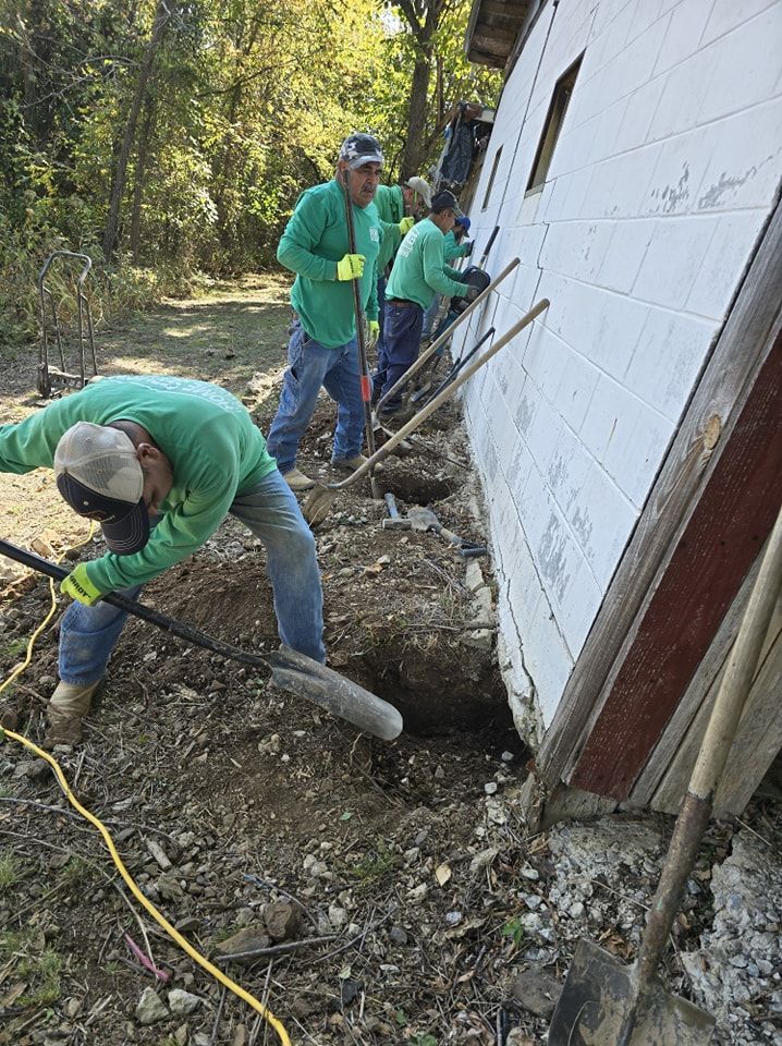 A wooden lakeside dock with tires hanging beneath a roofed structure, dirt foreground, and trees in the distance.