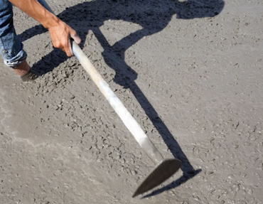A construction worker applies concrete, focusing on foundation leveling at the site.