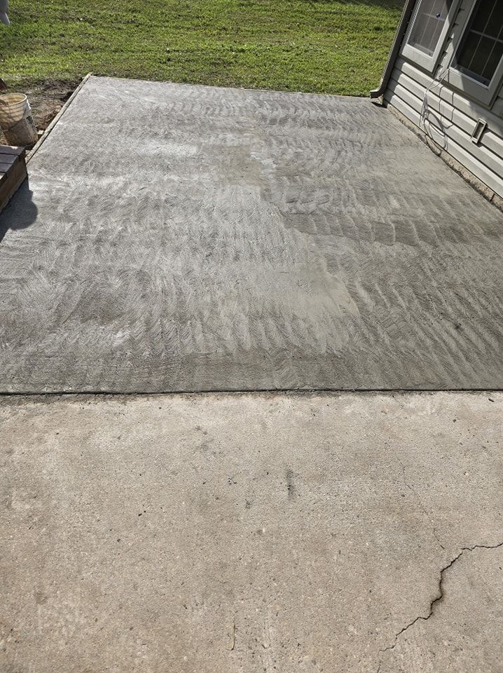 A gray concrete patio next to a light gray, cracked concrete path, with grass in the background.